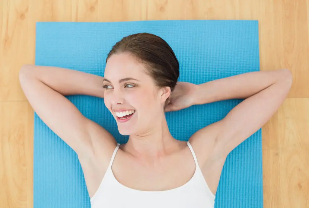 5 Ways exercise can make you happy. Image of cheerful woman lying on an exercise mat