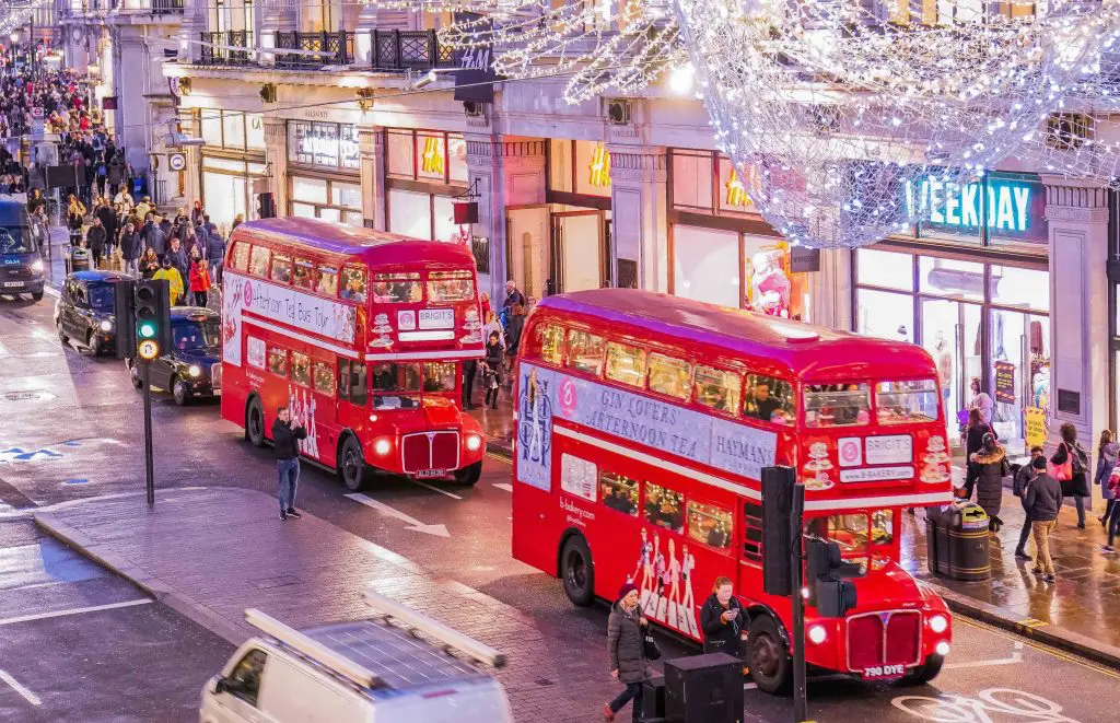Happy Days: London Afternoon Tea Bus Tour. Image of Afternoon Tea Tour buses on a London high street with the Christmas lights above