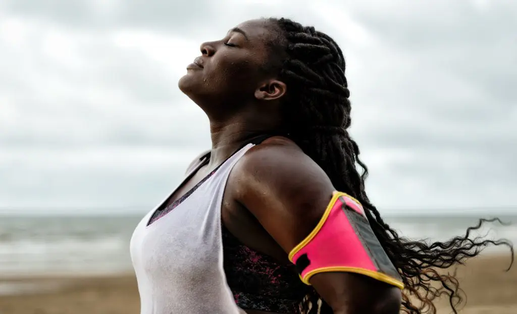 How to start running: tips for beginner runners. Image of woman standing with her eyes closed and head back breathing and regrouping after a run on the beach