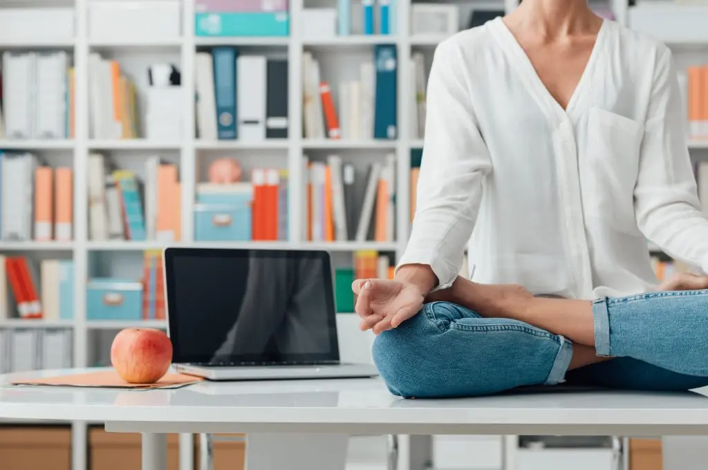 5 Useful ways mindfulness helps in your everyday life. Image of a Relaxed woman practicing meditation at home, she is sitting in the lotus position on the office desk, mindfulness concept