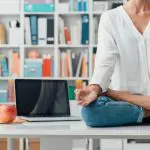 5 Useful ways mindfulness helps in your everyday life. Image of a Relaxed woman practicing meditation at home, she is sitting in the lotus position on the office desk, mindfulness concept