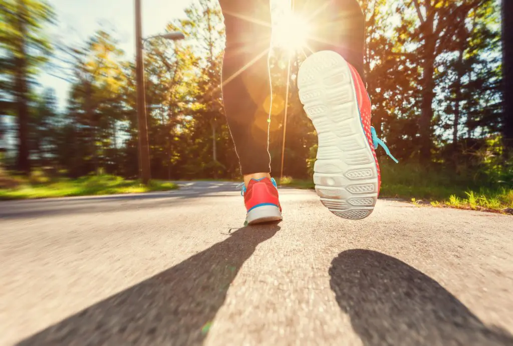 How to start running: Tips for beginner runners. Image of Female runner jogging down the road at sunset