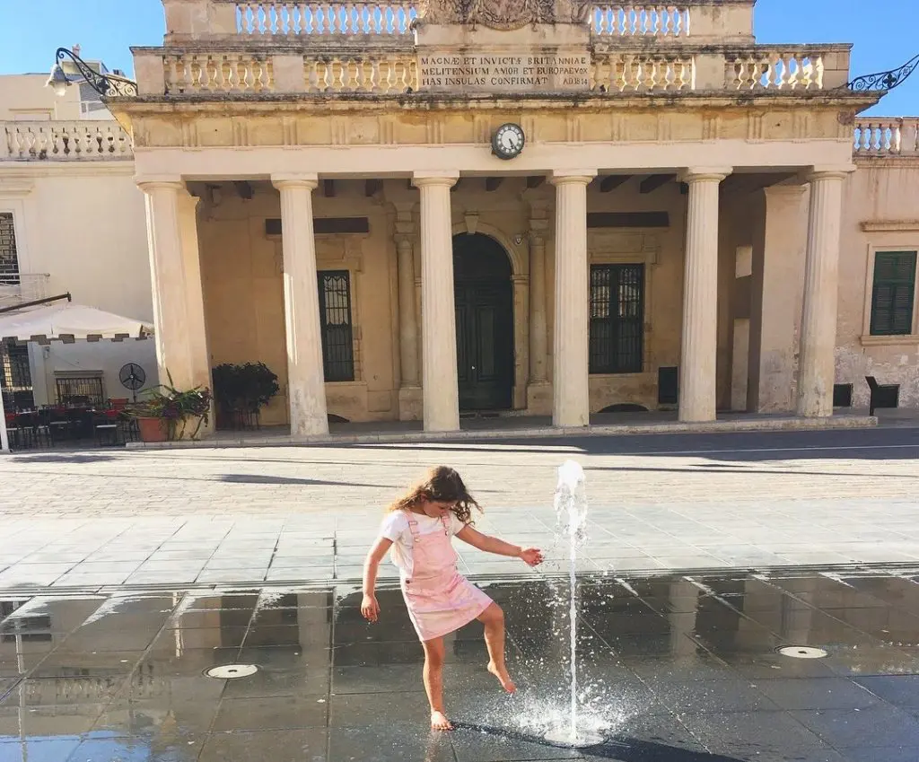 Fun things to do in Malta with kids. Image of young girl playing by a water fountain in Valletta Malta.