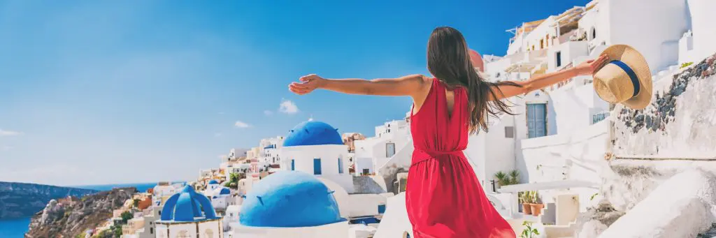 Happy Holidays: How to make your holiday even happier. Feel happy on holiday. Image of Europe travel vacation fun summer woman feeling free dancing with arms open in freedom at Oia, Santorini, Greece island. Carefree girl tourist banner panorama.