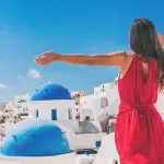 Happy Holidays: How to make your holiday even happier. Feel happy on holiday. Image of Europe travel vacation fun summer woman feeling free dancing with arms open in freedom at Oia, Santorini, Greece island. Carefree girl tourist banner panorama.