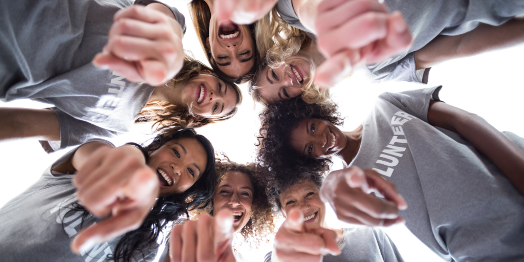 Feeling good for doing good: Why volunteering benefits everyone. Image of a group of females wearing grey t-shirts saying volunteer, smiling and pointing at the camera