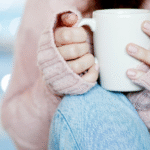 Woman in pink jumper and blue jeans holding a white mug feeling cosy self-care practice