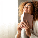 Feature Image for the Post How to Build Emotional Resilience. Woman is smiling looking content whilst holding up a notebook