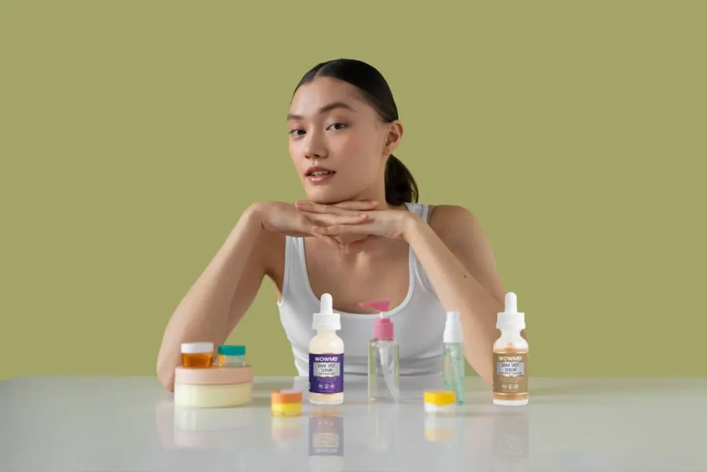 Top 5 Dark Spot Correctors For All Skin Types, Recommended By Dermatologists. Woman sitting at a desk with different skincare products surrounding her