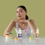 Top 5 Dark Spot Correctors For All Skin Types, Recommended By Dermatologists. Woman sitting at a desk with different skincare products surrounding her