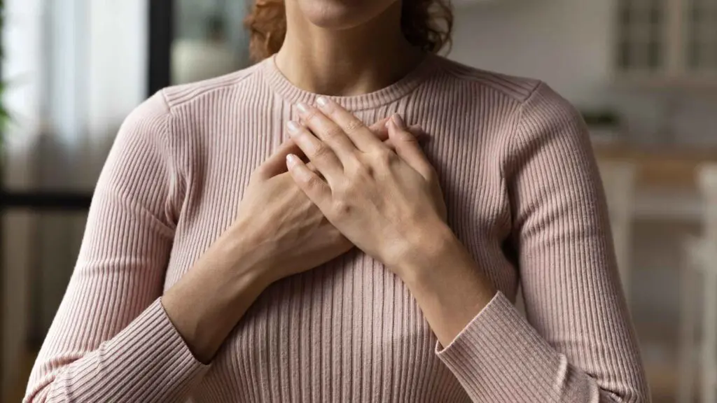 A woman in a jumper holding her hands to her heart to illustrate nervous system reset routines