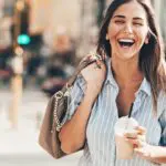 Happy Smiling Woman walking along the street carrying her handbag and a frappe, concept of having a happy day