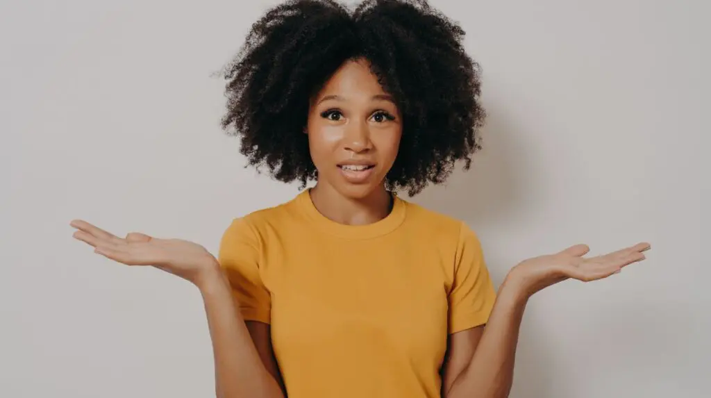 Woman in yellow t-shirt shrugging her shoulders and holding her hands up as it to say she doesn't know something