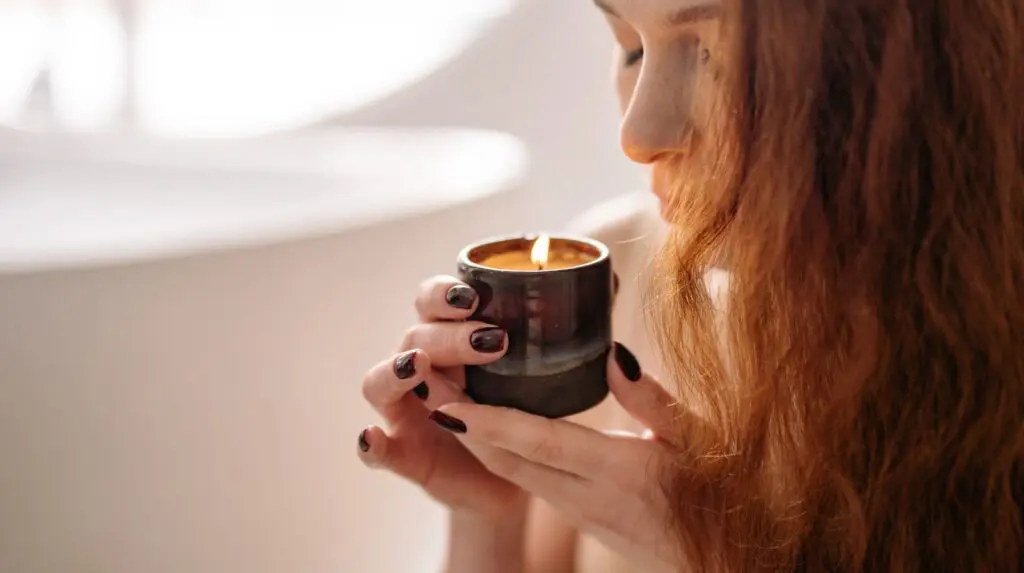 Woman Smelling a lit candle. Creating an end of the day ritual is one simple way to make your day easier