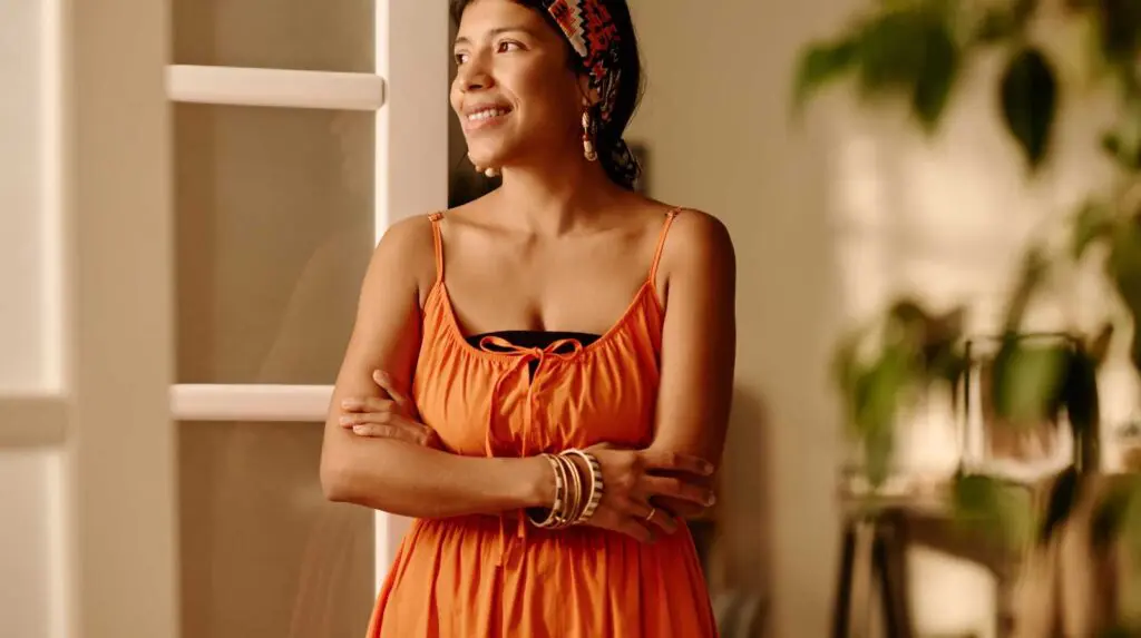 A woman stands inside a home with her arms folded looking happy and confident having completed a future self exercise
