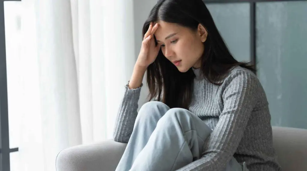 Woman sitting on sofa with her head resting on her hand symbolising anxiety and lifestyle changes for anxiety that are required