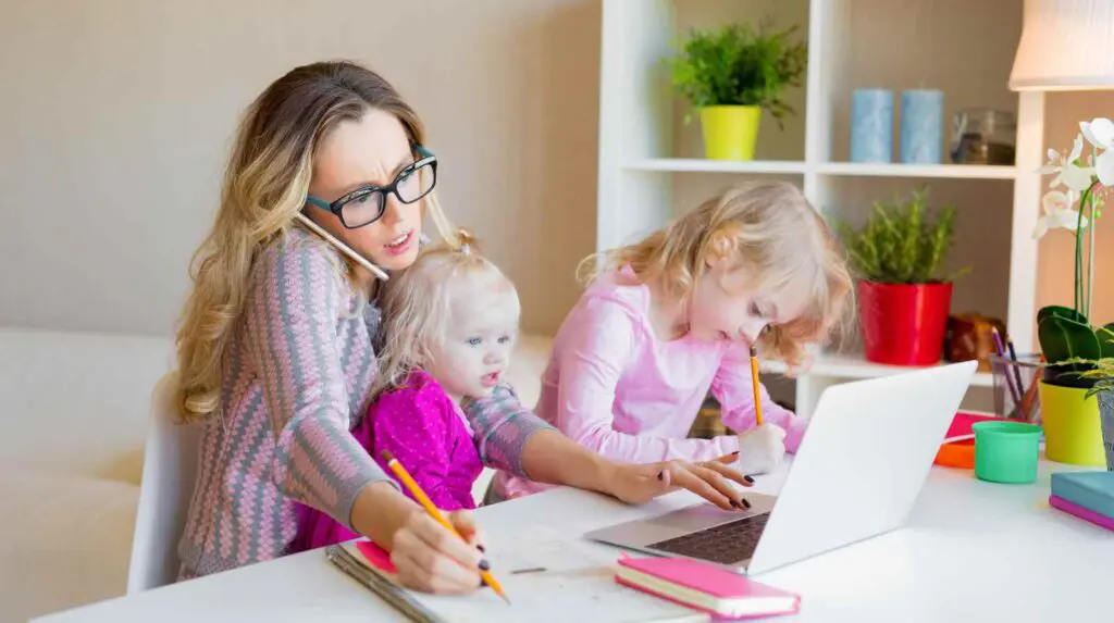 woman multitasking at a desk working with two young children concept of overworked and in need of radical rest