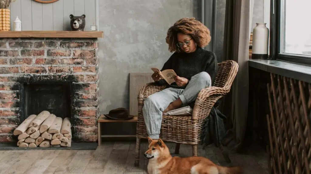 Woman sitting in a chair reading with a dog at her feet concept of radical rest
