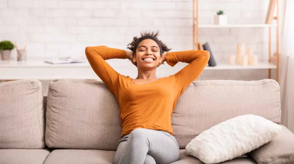How your home affects your mood (and simple ways to feel calmer instantly) Happy Woman sitting on a sofa in a organised and clean room