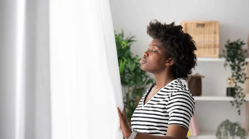 Woman at window facing sunlight and practising deep breathing to help aid relaxation