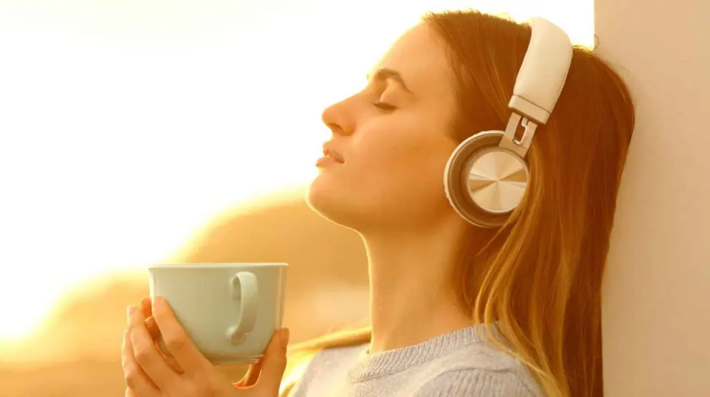 Woman on a balcony listening to music and breathing deeply whilst holding a mug of drink