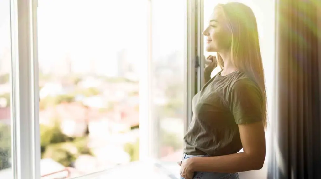 Woman standing by open window allowing fresh air into her home