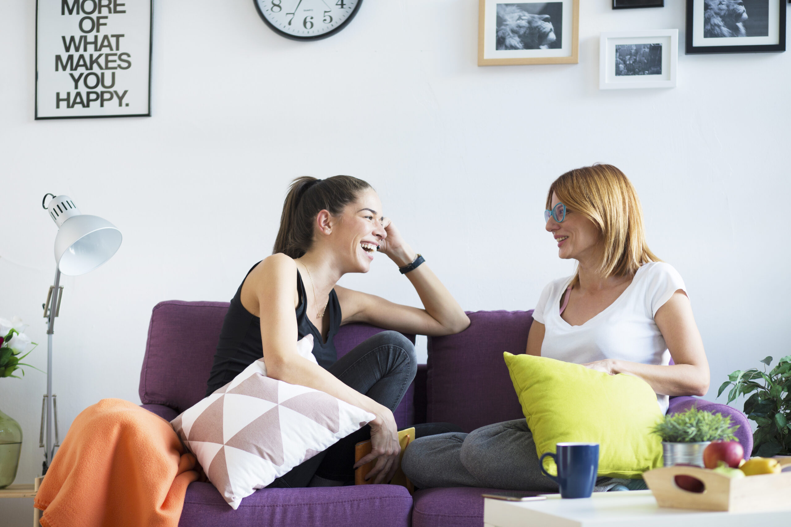 How to be more positive - Two happy young female friends conversing in the living room at home