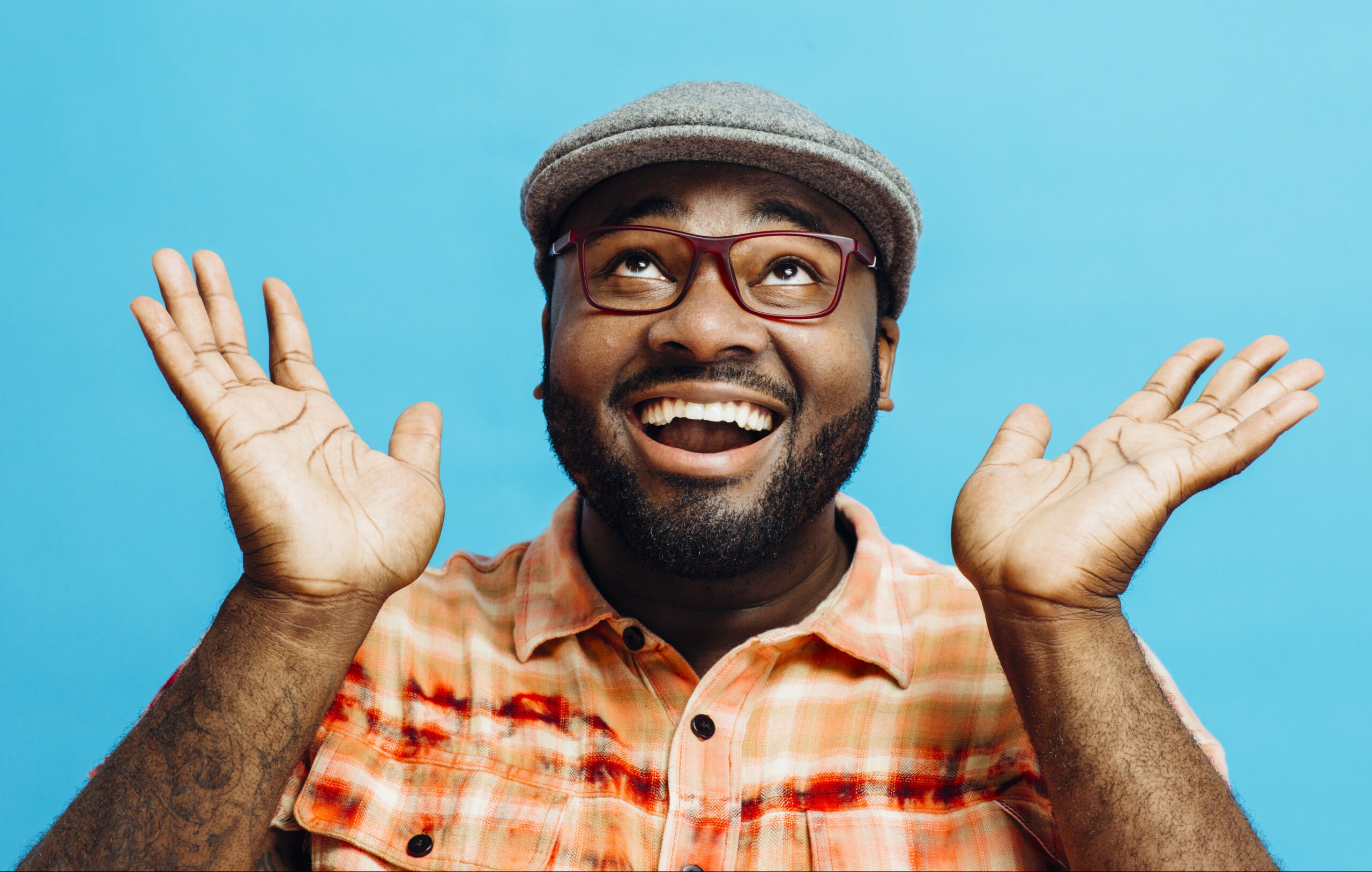 Improving well-being: The key to being happy? Image of man wearing a flat cap and glasses, smiling, looking upwards and holding up his hands in a happy gesture
