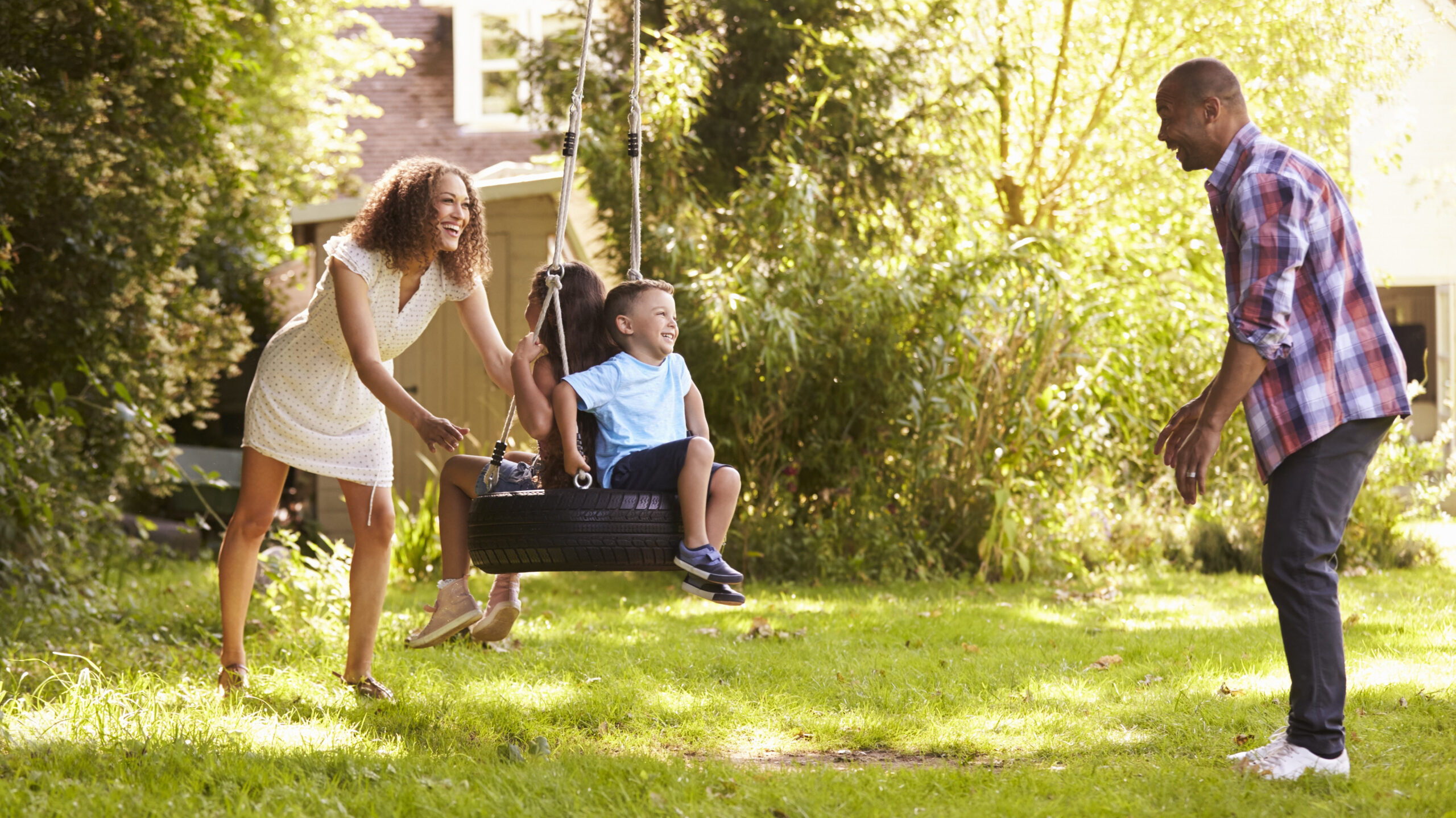 Exercise Hacks: How to be fitter without really trying. Image of parents pushing children on tire swing in a garden