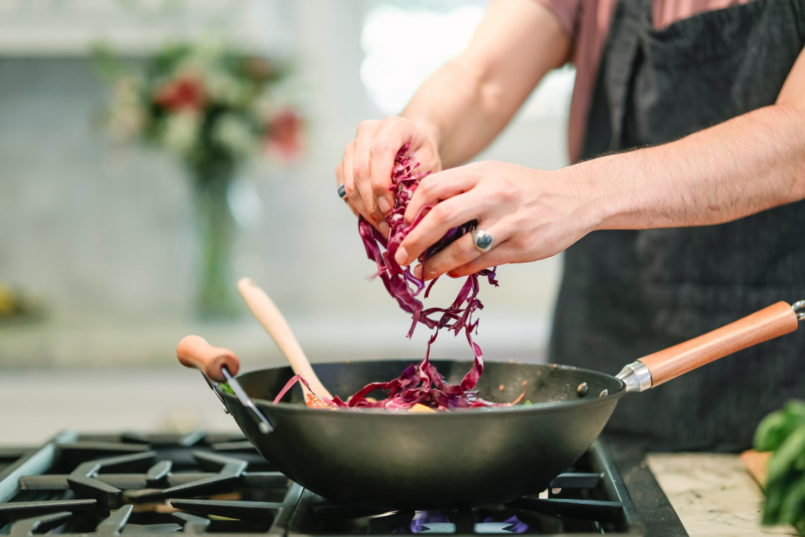 Exercise Hacks: How to be fitter without really trying. Image of an adult male putting shredded red cabbage into a wok cooking on a stove