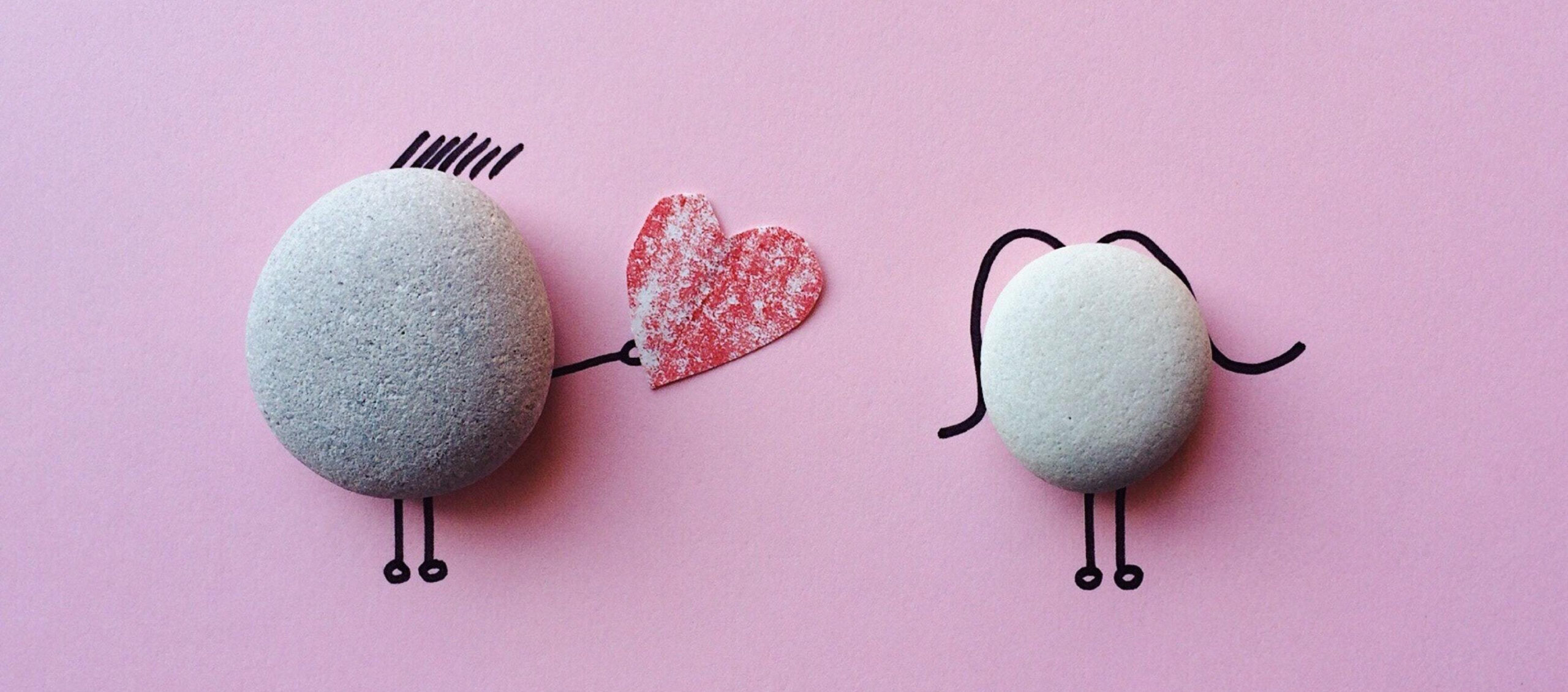 5 Useful ways mindfulness helps in your everyday life. Image of two pebbles with black marker illustrations to depict a male and female - the male is offering the female a red paper heart