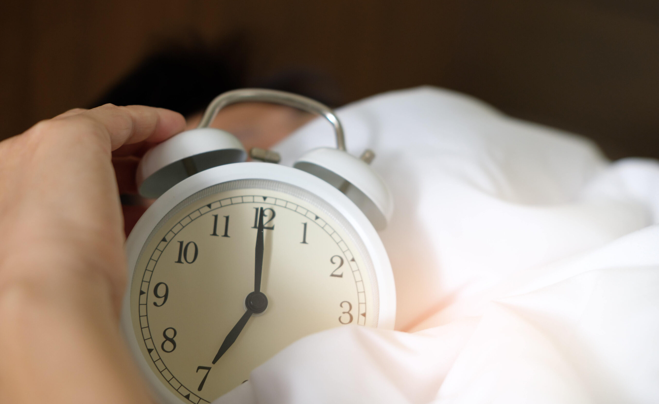 Sleep well: How to win at sleeping! (and why you should want to). How to get a better night's sleep. Image of an adult male holding an alarm clock on top of a duvet