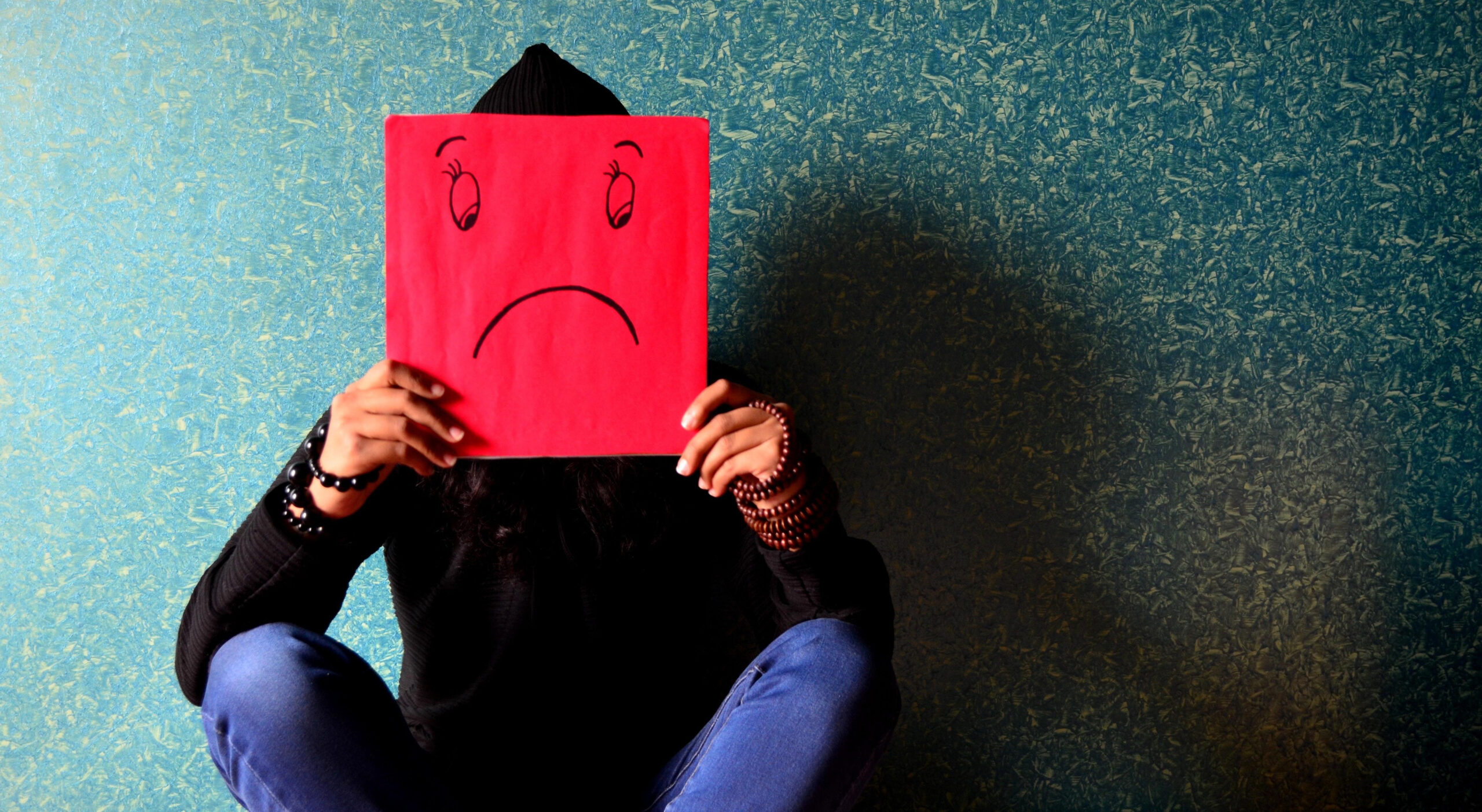 Sleep well: How to win at sleeping! (and why you should want to) How to get a better night's sleep image of a person crouching against a wall holding up a unhappy face picture over their face
