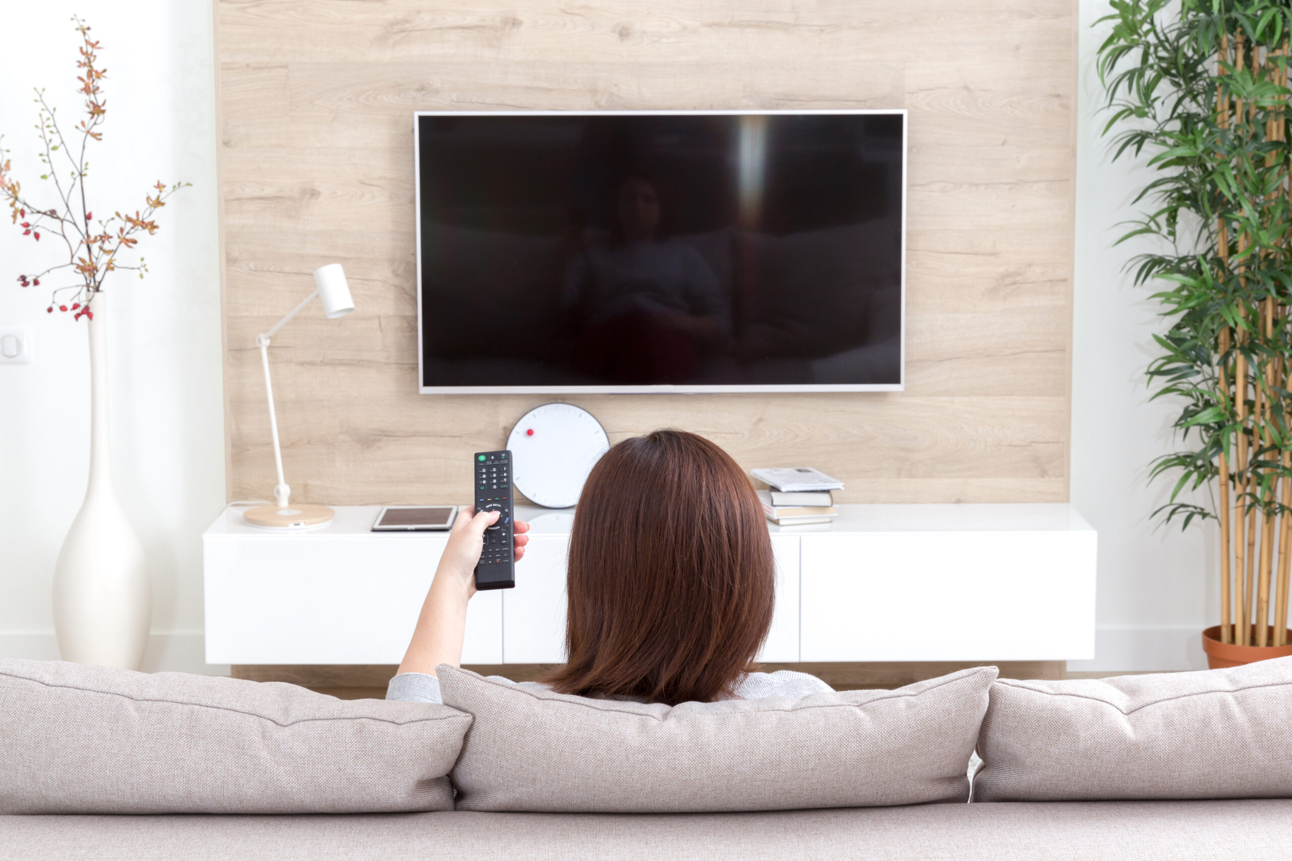 How to stop catastrophizing, avoid triggers. Image of Young woman watching TV in living room, back view
