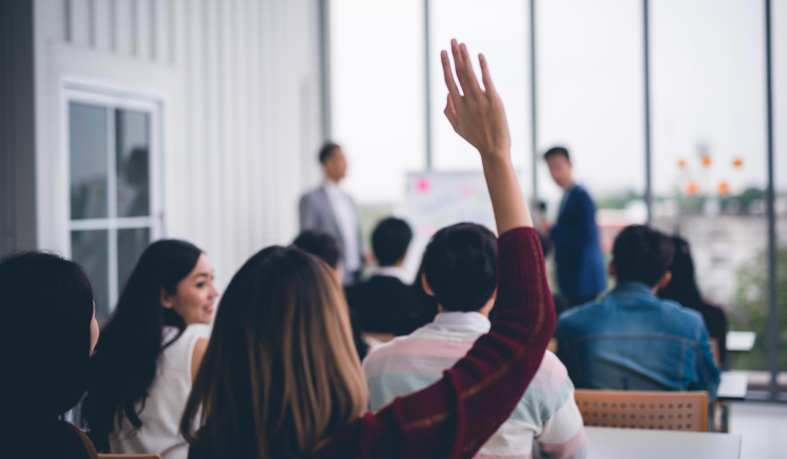 Feeling good for doing good: Why volunteering benefits everyone. Image of woman raising her hand in an office environment to volunteer