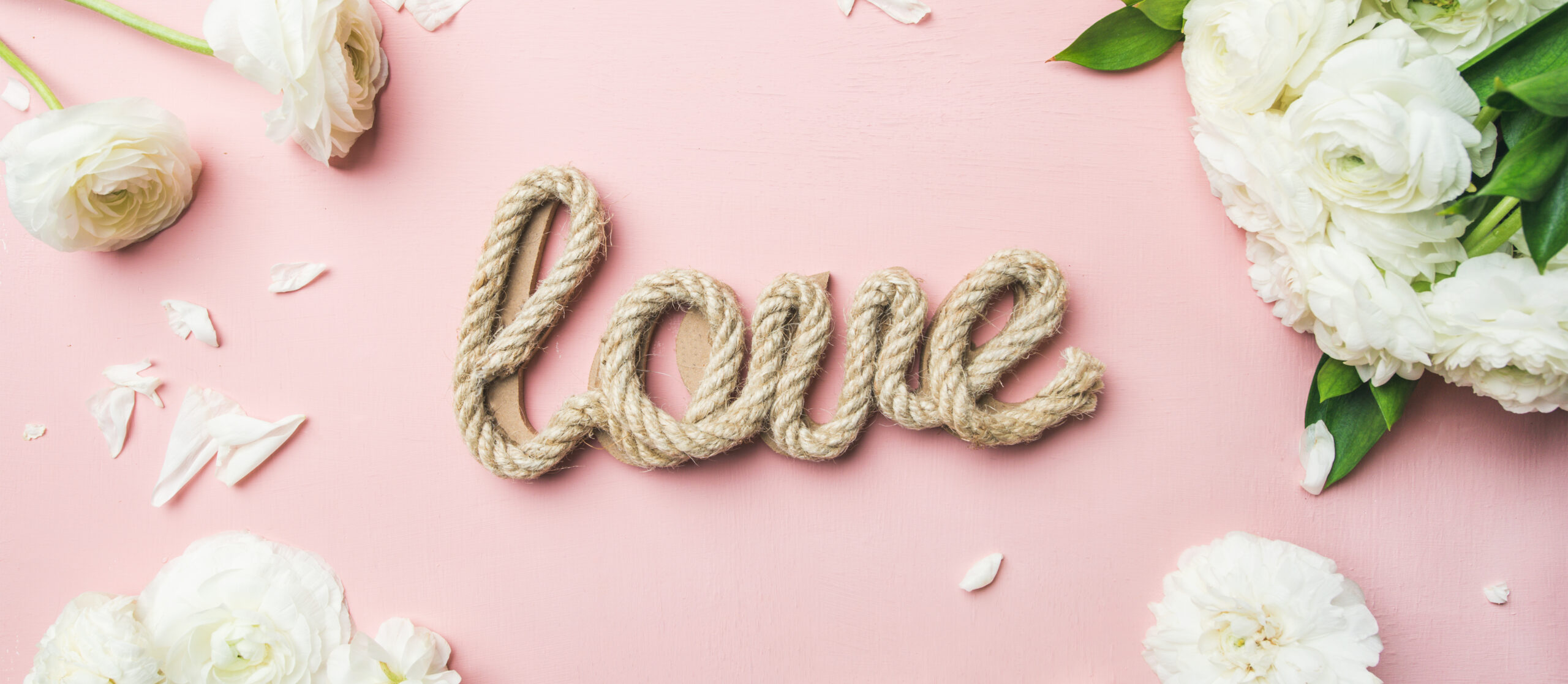 4 Tips to reduce wedding planning stress. Image of Saint Valentines Day background. Flat-lay of white ranunculus flowers and word love over light pink background, top view, wide composition. Greeting card or wedding invitation