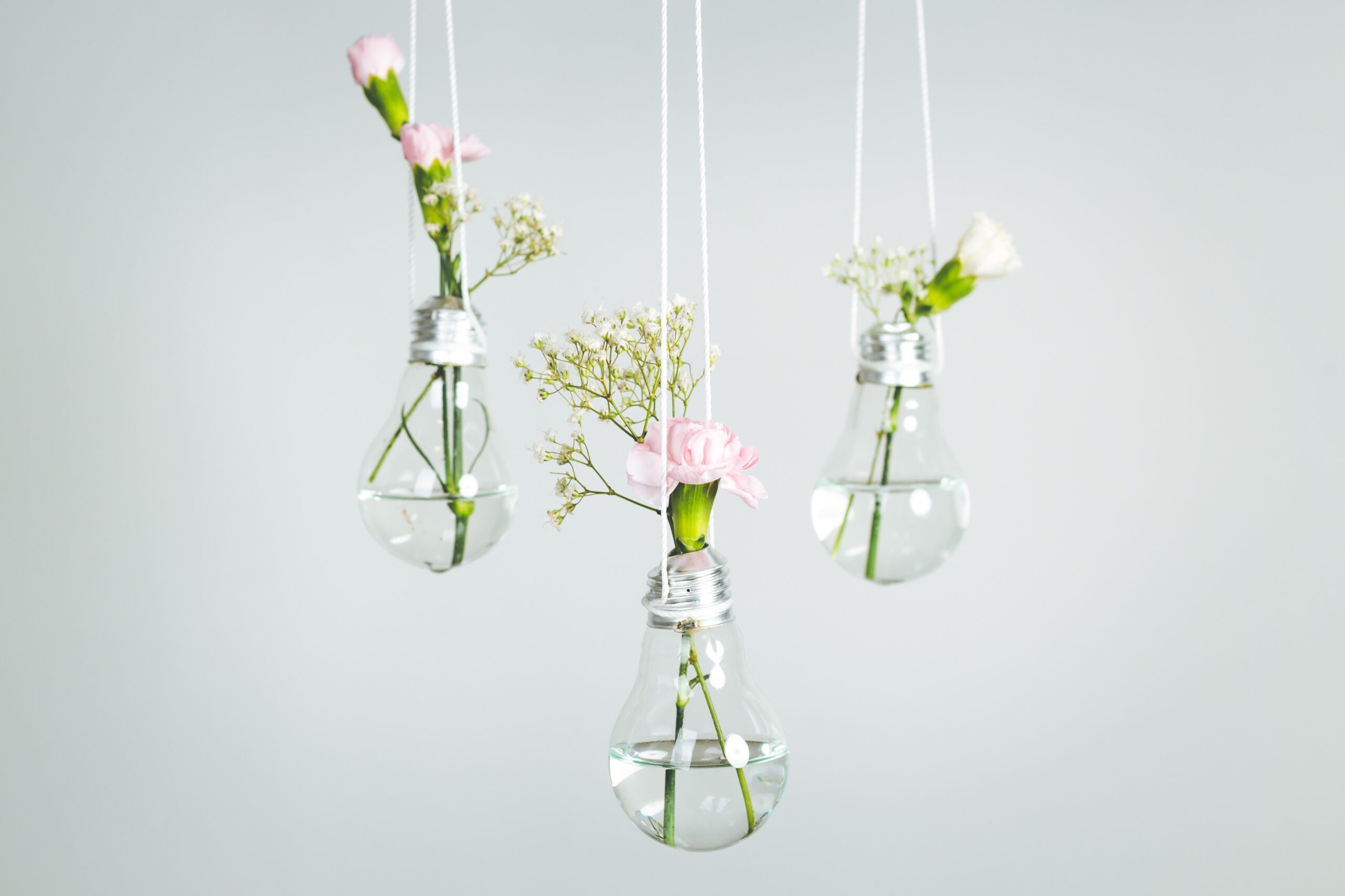 4 Tips to reduce wedding planning stress. Image of 3 lightbulb vases with a carnation & sprig of baby's breath in each one. Each vase is suspended in the air by string