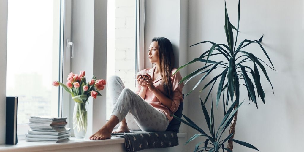 Woman sitting in window with a drink looking out of window, thinking