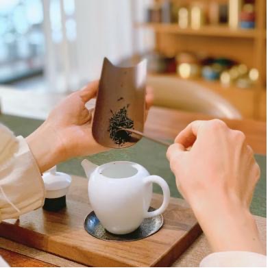 Person transferring tea leaves into a small teapot using a tea funnel and tea spoon as part of a mindful tea ritual
